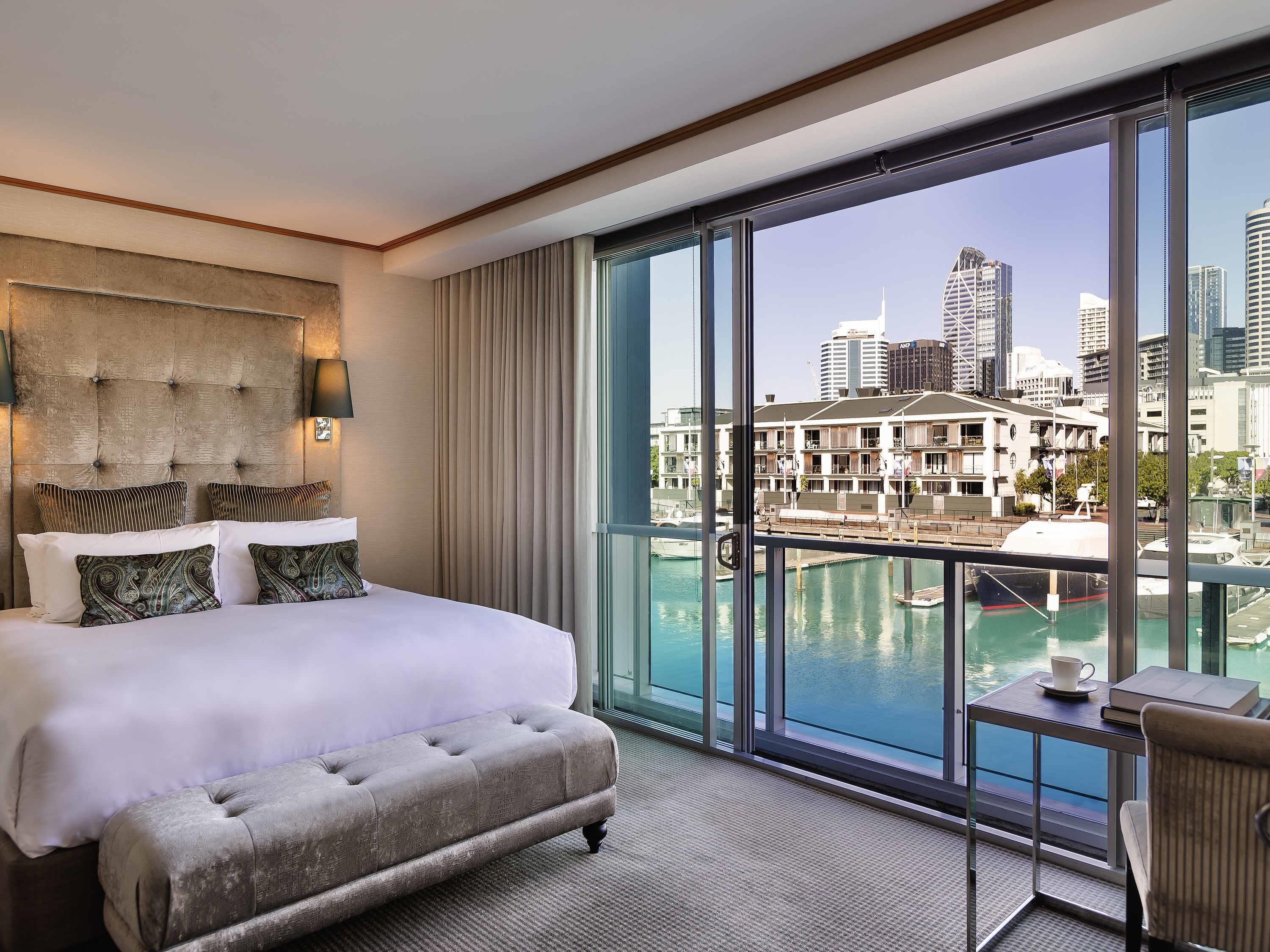 A hotel room with a large bed, a tufted headboard, a view of a marina and city skyline.