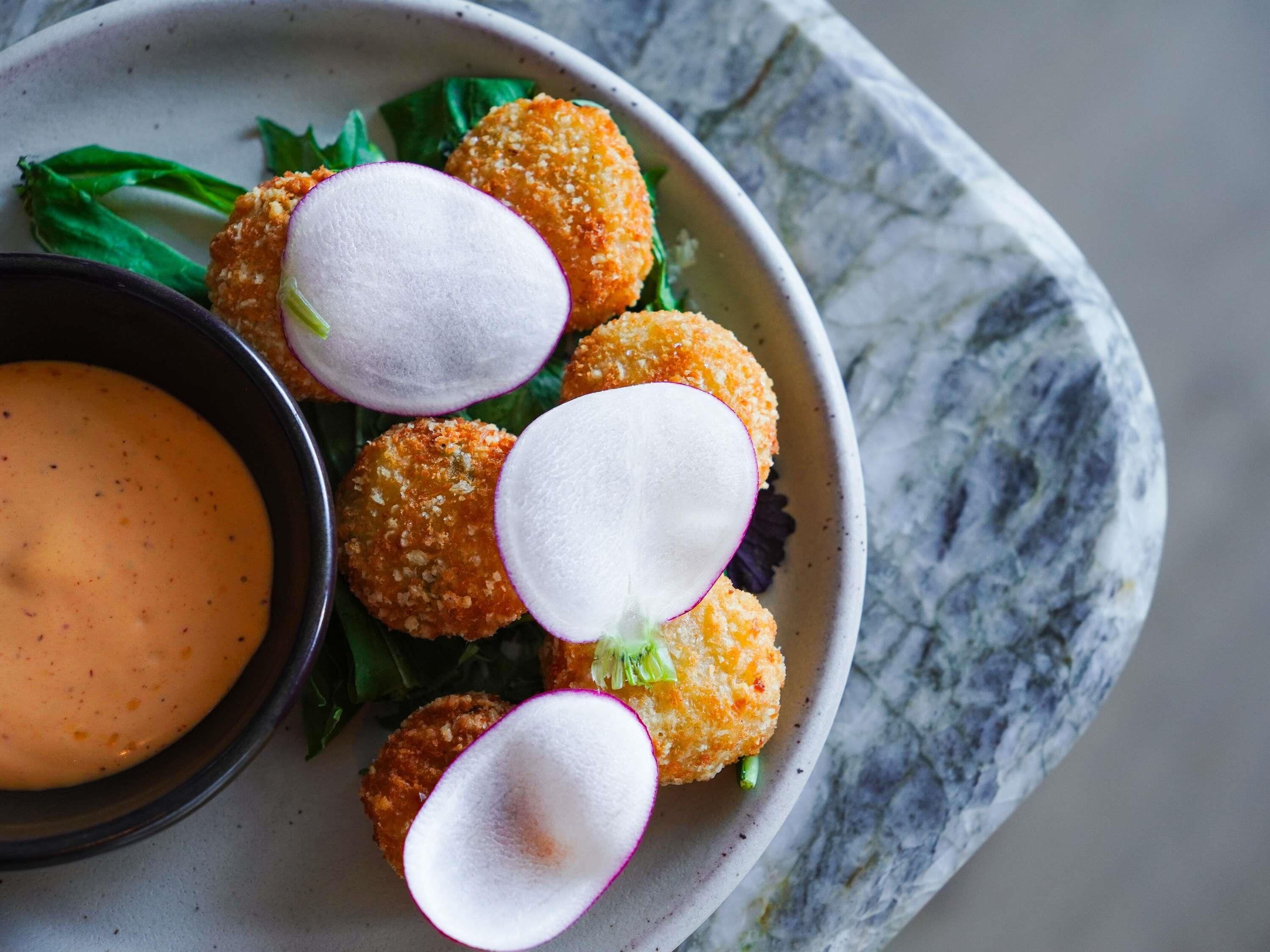 A plate with breaded items, radish slices, and a dipping sauce.