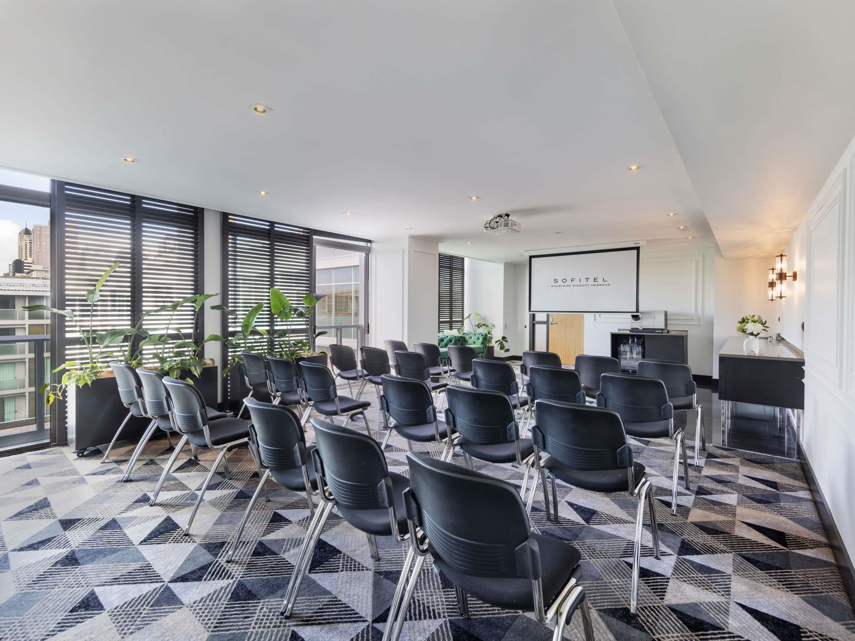 A conference room with rows of chairs, a projector screen, and a large window with blinds.