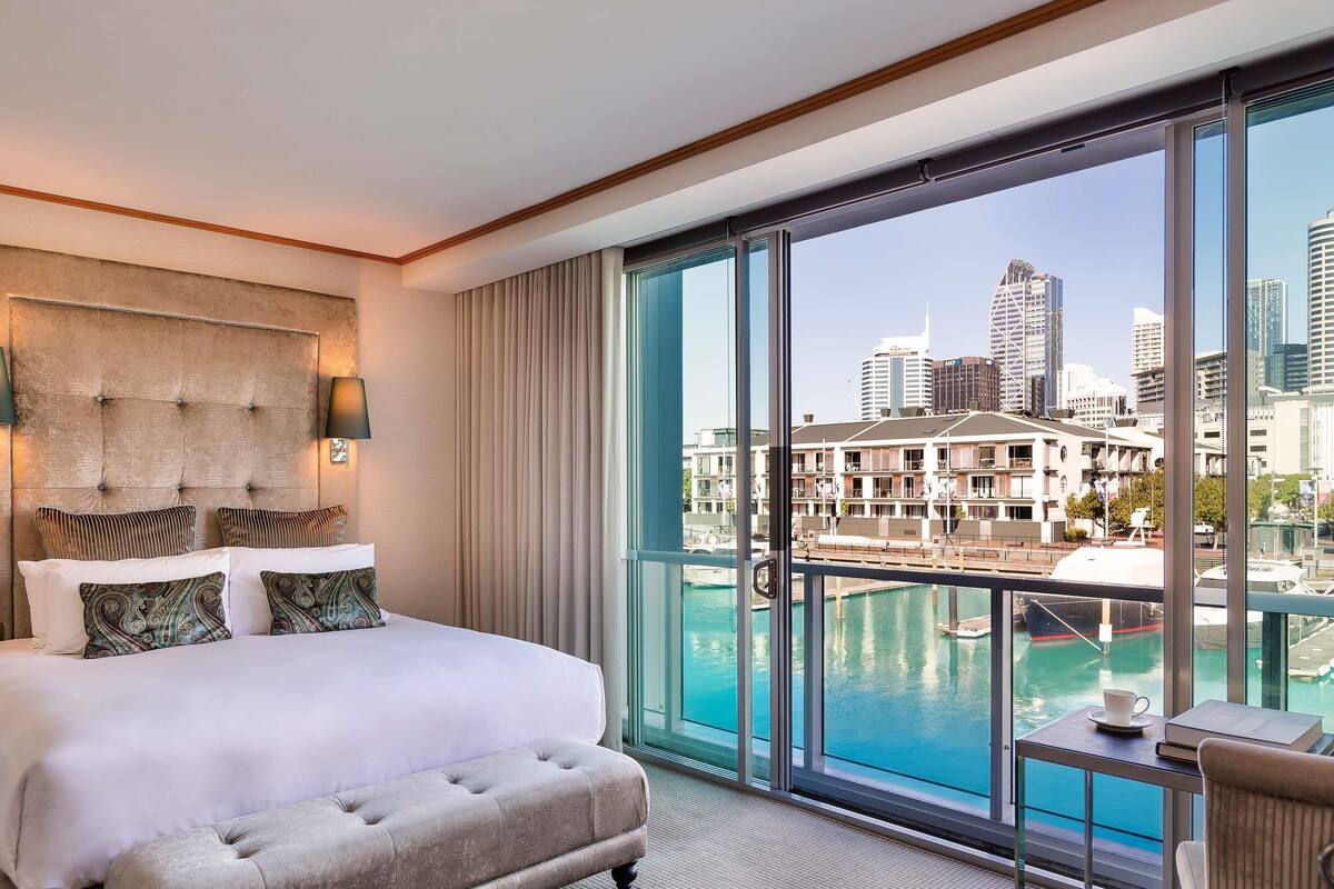 A hotel room with a large bed, a view of a city skyline, and a pool.
