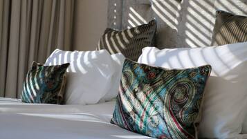 A bed with white linens and patterned pillows, a wall with a textured surface, and a window casting shadows.