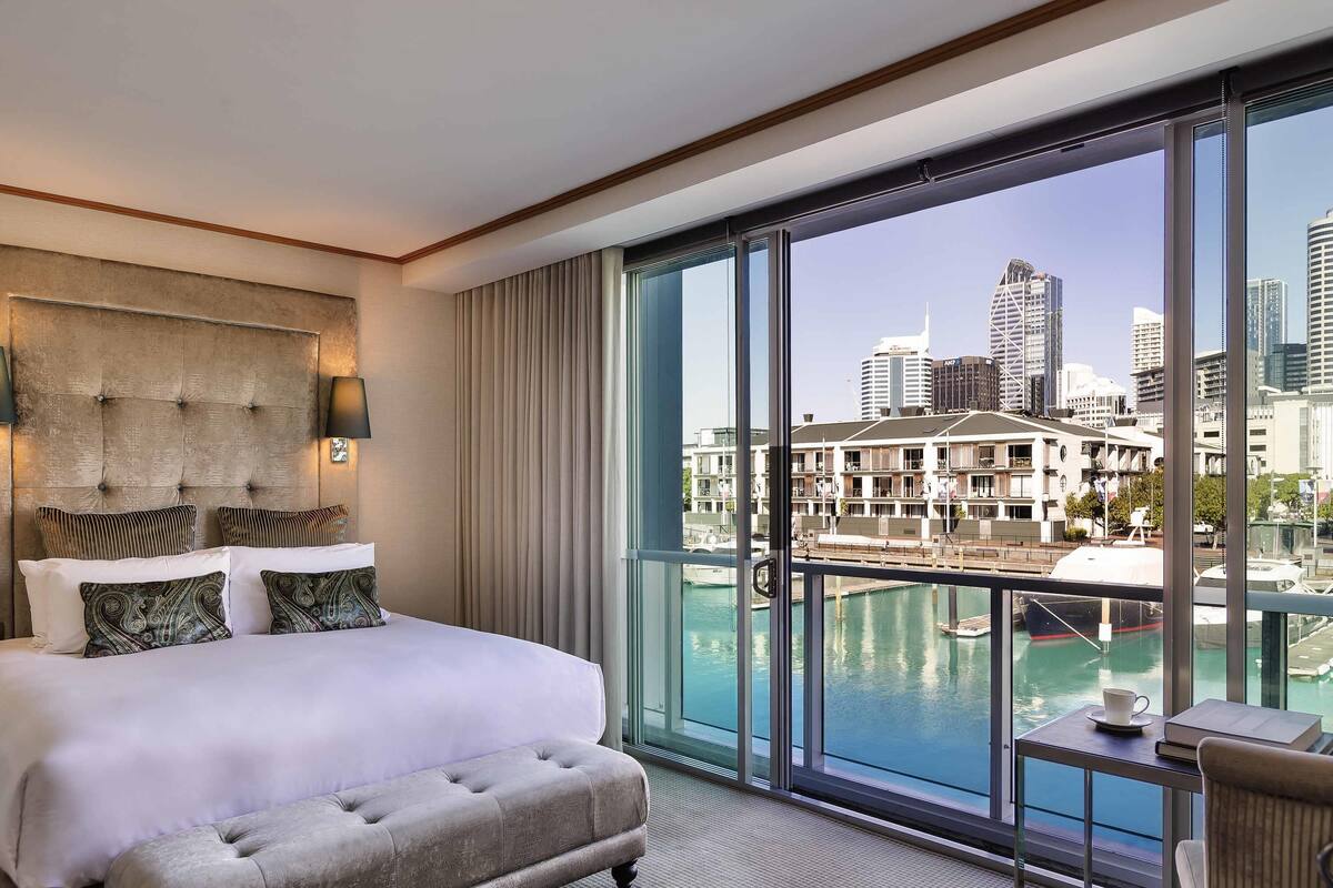 A hotel room with a large bed, a tufted headboard, a view of a marina and city skyline.