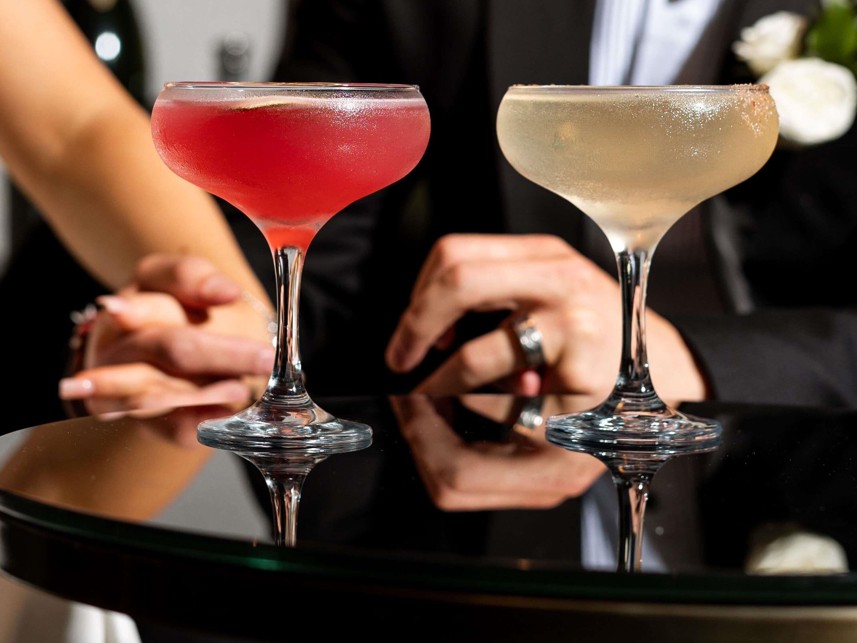 Two stemmed glasses on a reflective surface with a blurred background.