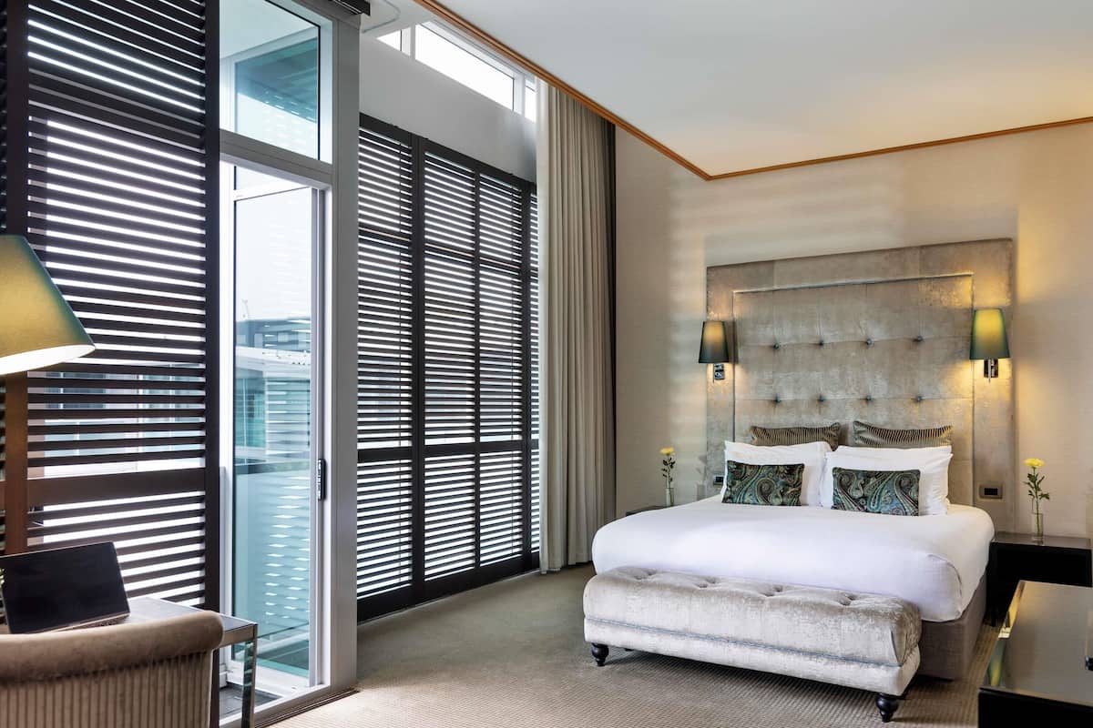 A modern hotel room with a large bed, a view through floor-to-ceiling windows, and a cityscape.