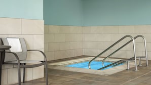 A pool area with a blue pool, metal pool ladders, and a chair with a towel.