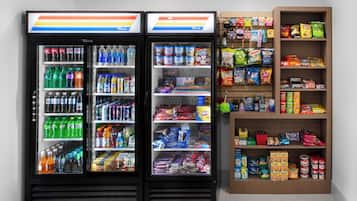 Dos dispensadores refrigerados con bebidas y aperitivos varios, y una estantería con alimentos envasados.
