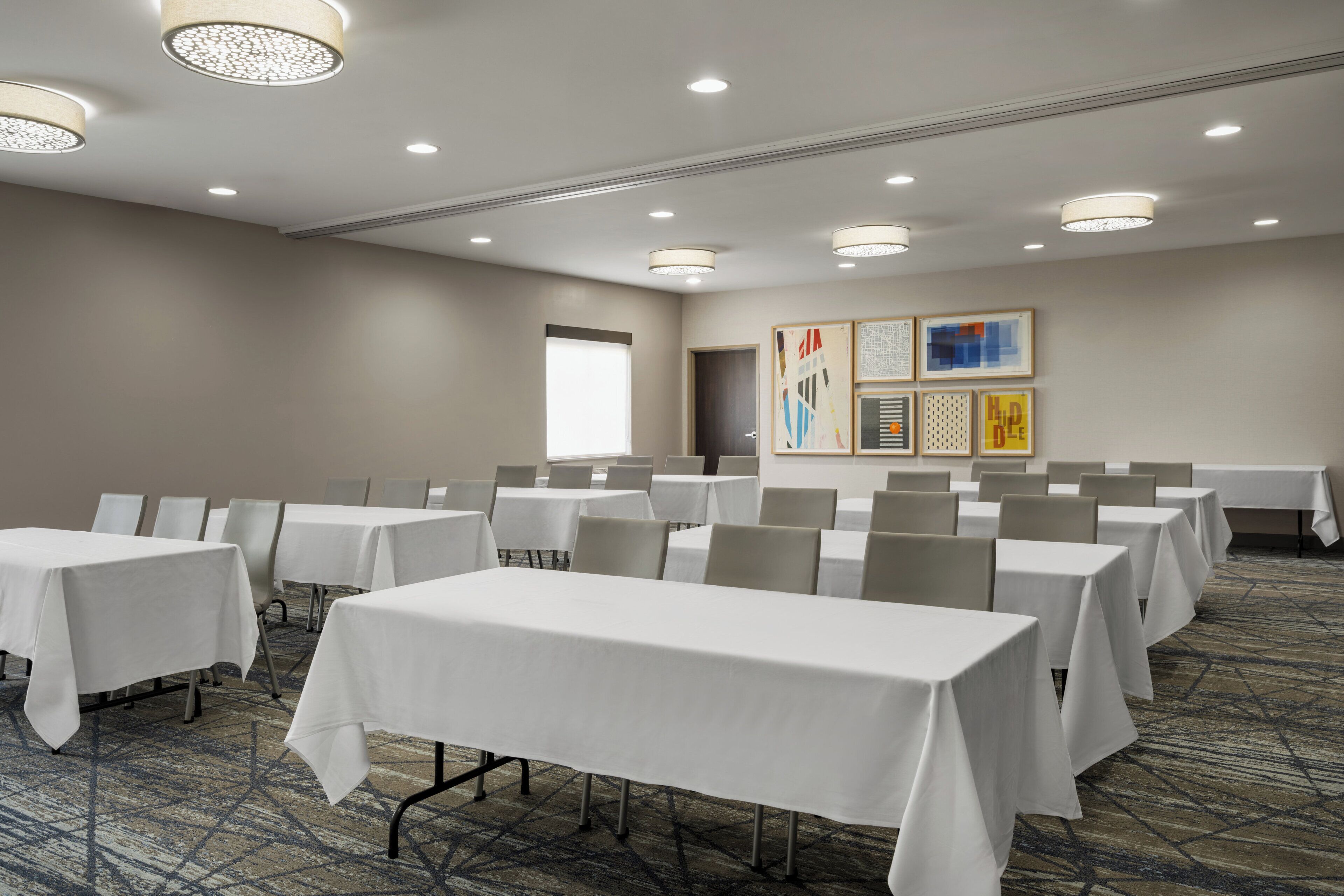 A conference room with multiple tables and chairs, a large window, and artwork on the wall.