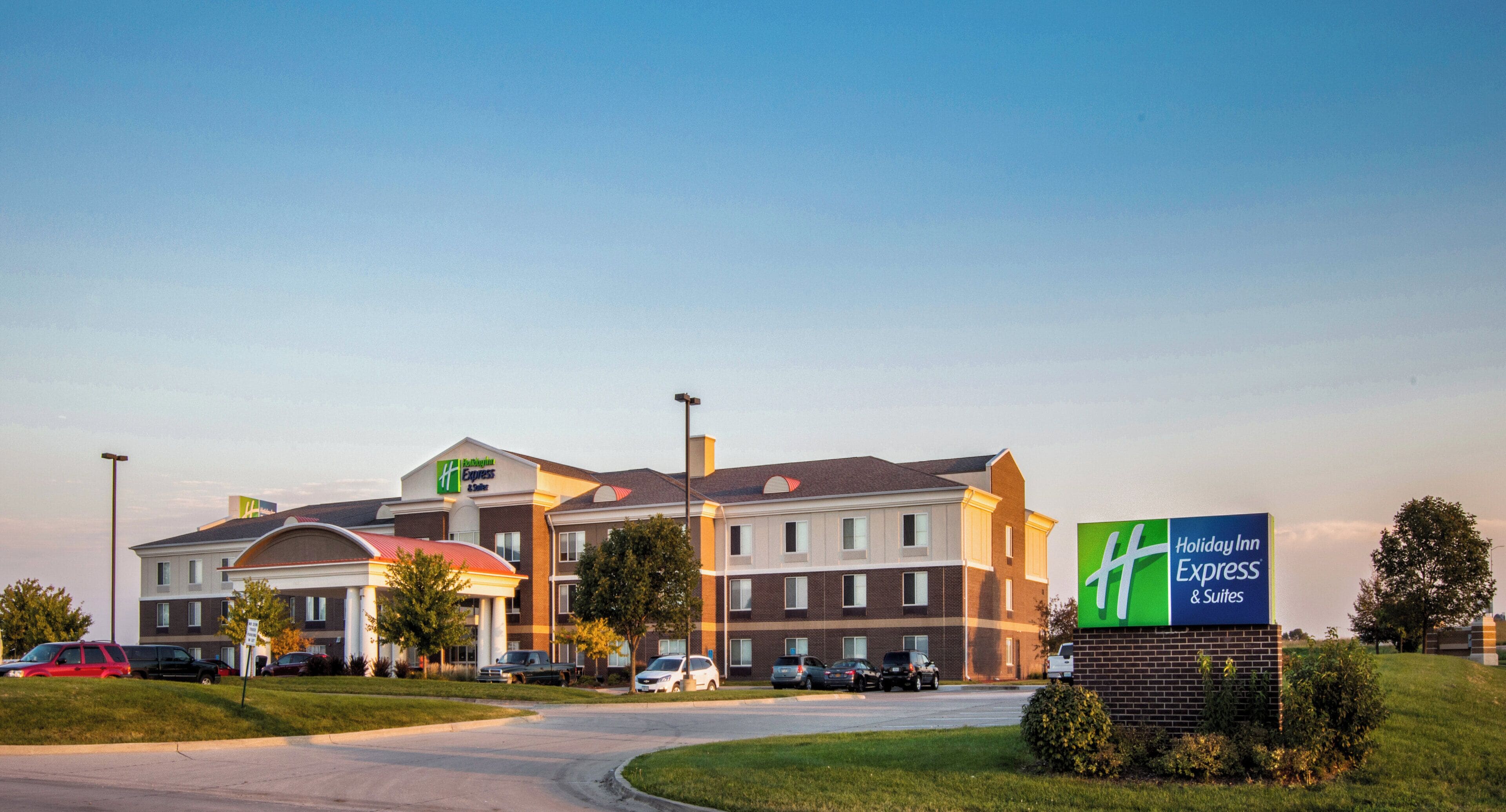 A Holiday Inn Express & Suites hotel with a brick facade, multiple windows, and a parking lot with several cars.