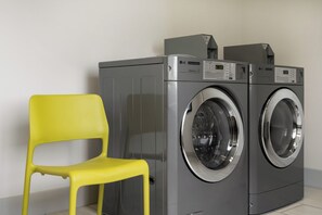 Dos lavadoras LG comerciales de carga frontal en un lavadero con una silla amarilla.
