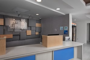 A modern hotel reception area with a grey and wood panel wall, a reception desk, and a blue counter.