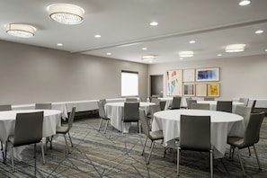 Un salón de conferencias con mesas redondas, sillas y piso alfombrado.