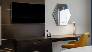 A modern hotel room with a flat-screen TV, a desk with a telephone, a chair, and a bed.
