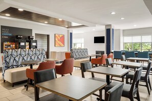Una cafetería moderna con mesas, una máquina de café y un televisor.