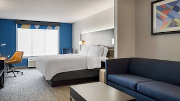A hotel room with a bed, a desk, a chair, a sofa, and a framed picture on the wall.
