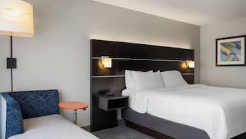 Quarto de hotel com cama, mesa de cabeceira, abajur e uma cadeira.