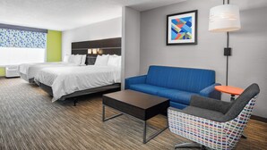 A hotel room with two beds, a sofa, a small table, a chair, a lamp, and a framed picture on the wall.