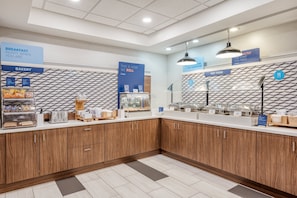 A clean, modern breakfast area with a bakery section, a hot food station, and a sign indicating breakfast is ready when you are.