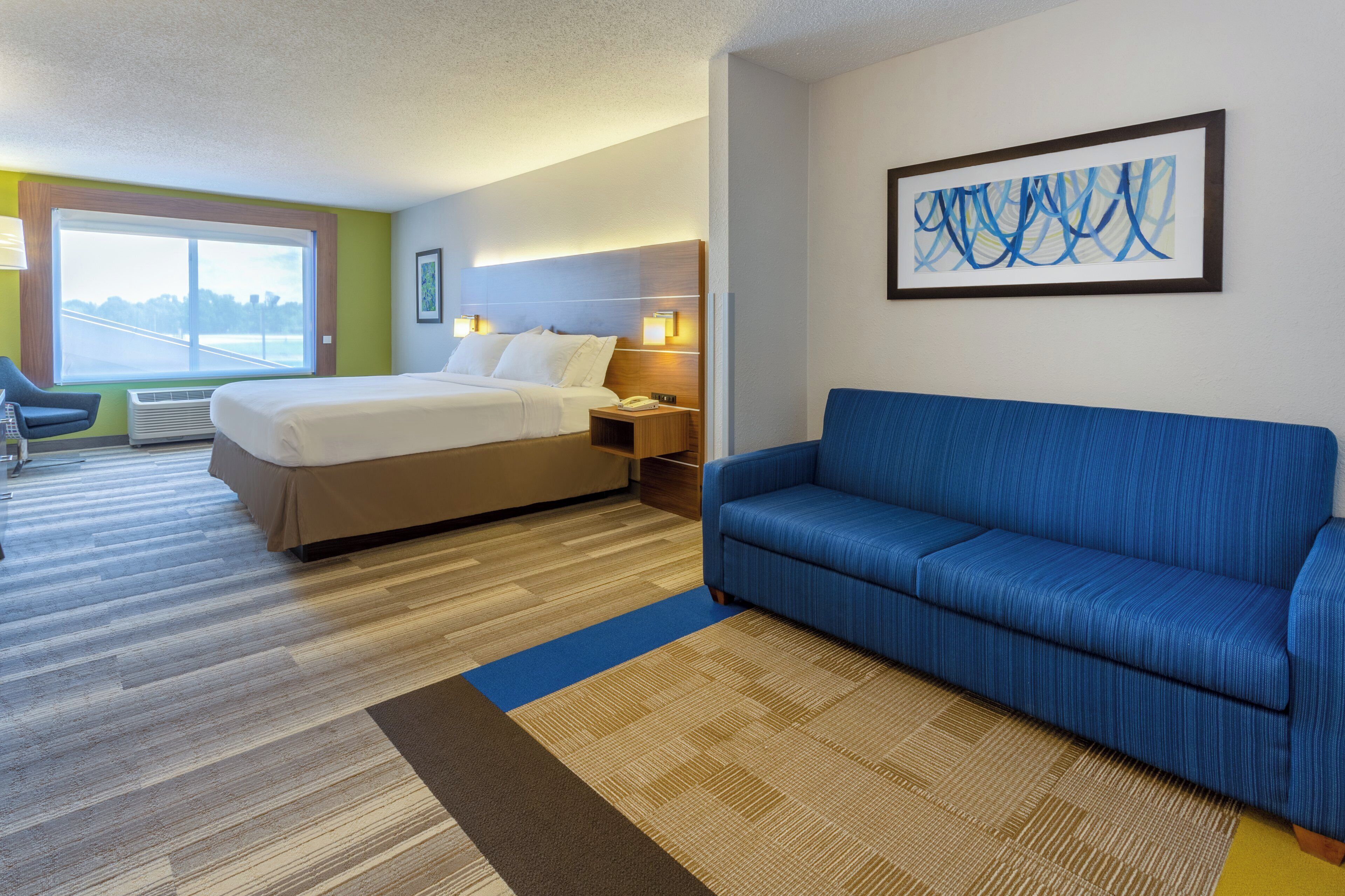 Habitación de hotel con cama, sofá azul, escritorio con lámpara y ventana con vista.