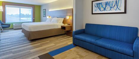 Habitación de hotel con cama, sofá azul, escritorio con lámpara y ventana con vista.