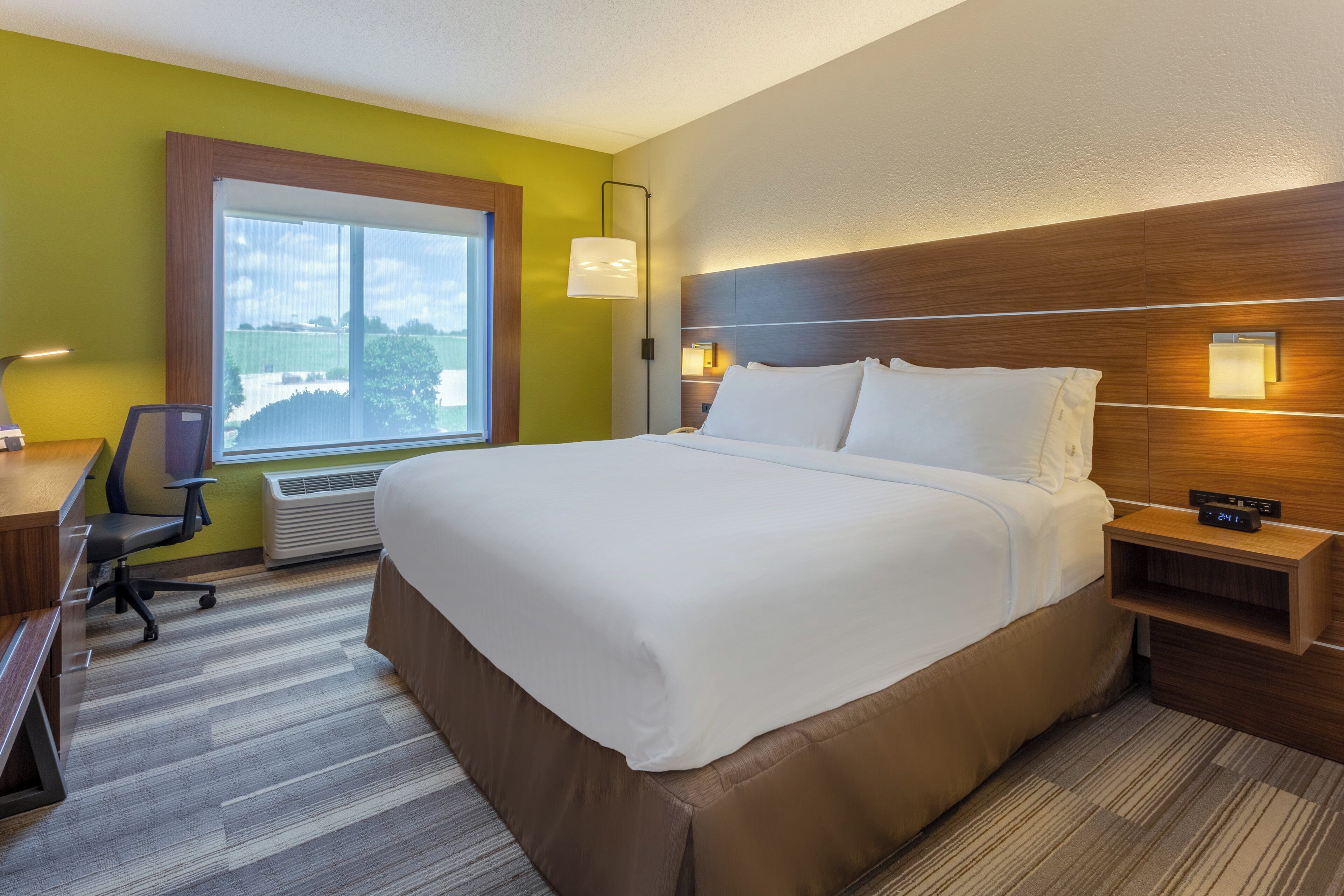 Habitación de hotel con una cama grande, un escritorio con silla, una ventana con vistas y una mesita de noche con lámpara.
