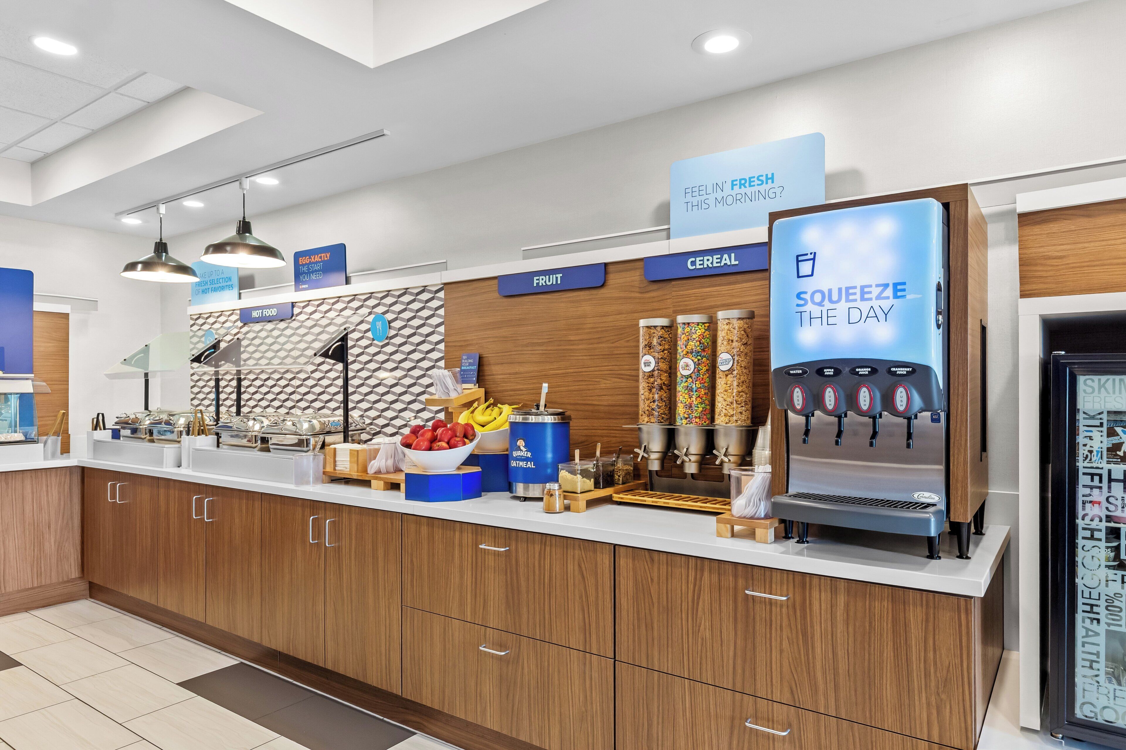 A modern breakfast bar with a cereal dispenser, fruit and hot food sections, and a water cooler.