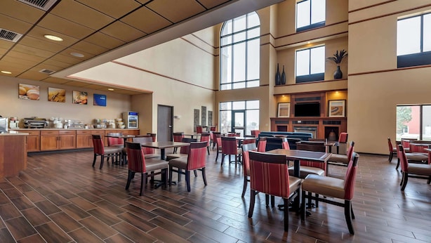 A spacious dining area with multiple tables and chairs, a kitchen area with a large window, and a counter with various food items. - Comfort Inn & Suites Goodland (Goodland)