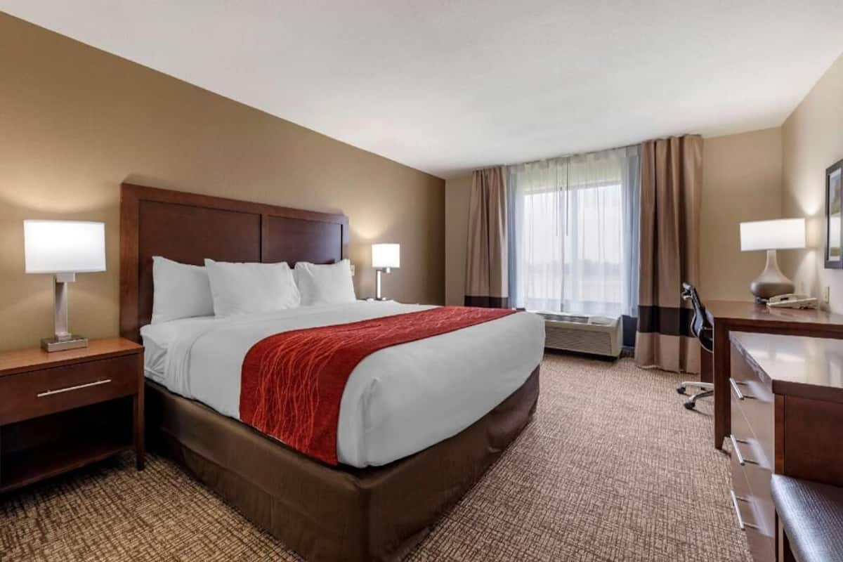 A hotel room with a large bed, two bedside tables with lamps, a desk, and an air conditioning unit.