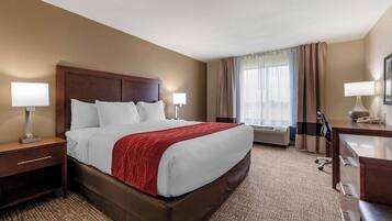 A hotel room with a large bed, two bedside tables with lamps, a desk with a chair, and a large window with curtains.