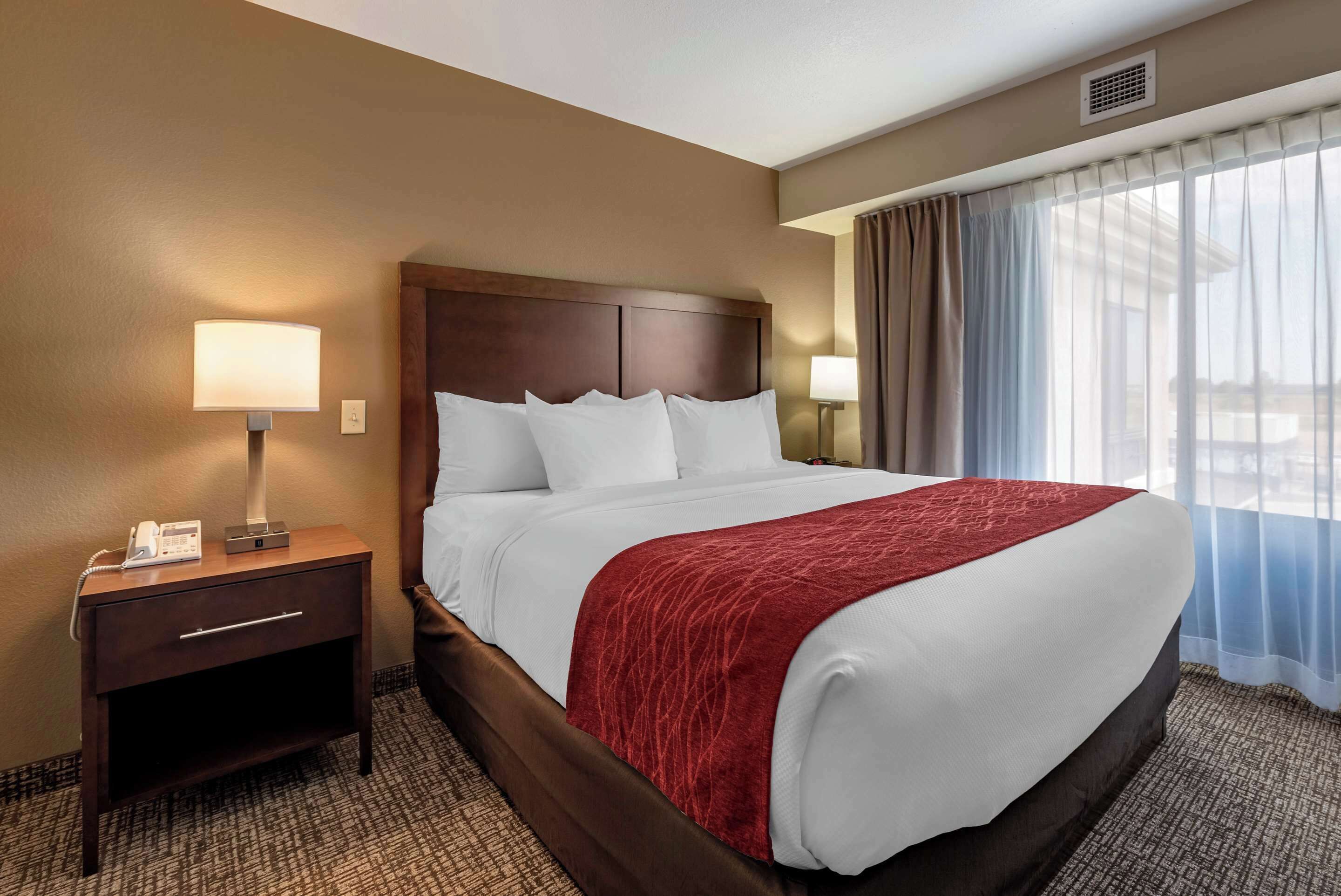 A hotel room with a large bed, a nightstand with a lamp, and a window with curtains.