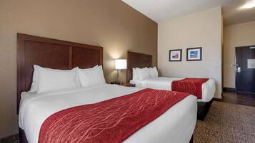 Habitación de hotel con dos camas, una colcha roja, una mesita de noche, una lámpara y dos cuadros en la pared.