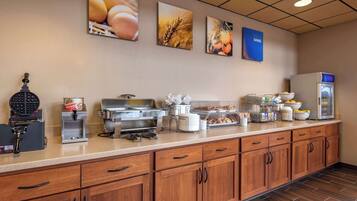 Ein Frühstücksbuffet mit Waffeleisen, Kaffeeautomaten und verschiedenen Speisen.