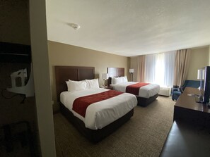 A hotel room with two beds, a desk, a TV, and a window with curtains.