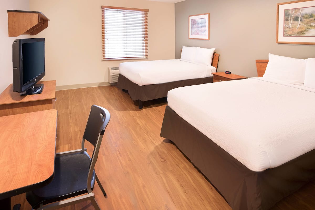 A hotel room with two beds, a desk with a chair, a television, and a window with blinds.