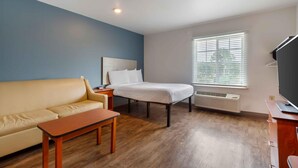 A room with a bed, a sofa, a small table, a desk with a computer, and a window with blinds. - Extended Stay America Select Suites - Fayetteville (Fayetteville)