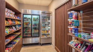 A narrow hallway with a refrigerator stocked with beverages and snacks, adjacent to shelves filled with various food items and toiletries. - Holiday Inn Express and Suites Modesto by IHG (Modesto)
