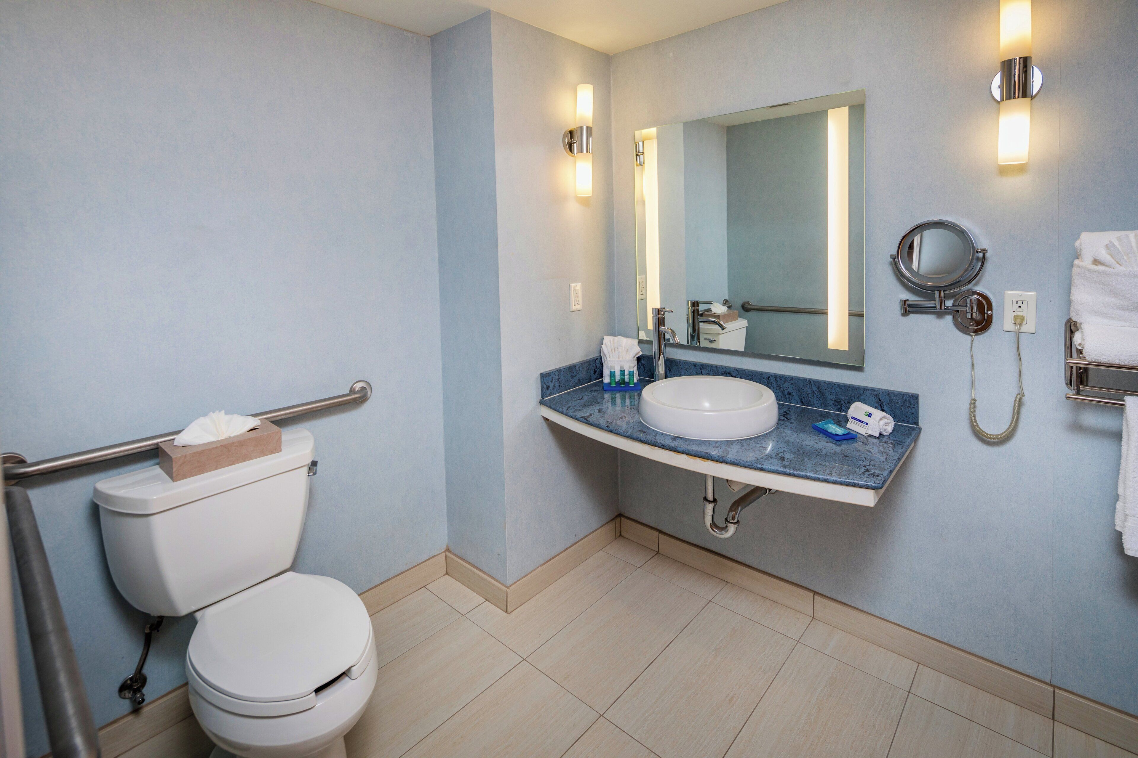 A bathroom with a toilet, sink, mirror, and handrails.