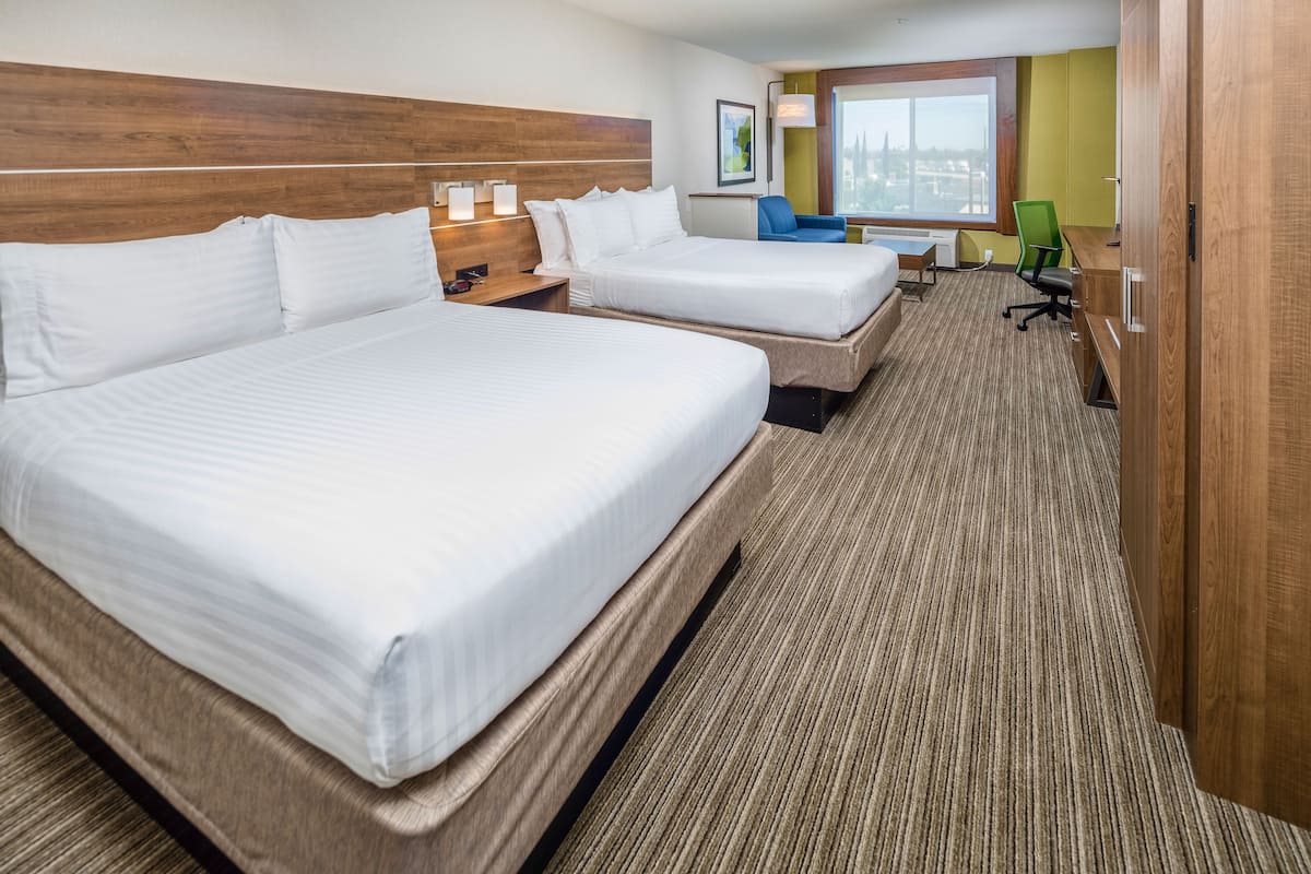 A hotel room with two beds, a desk, a chair, and a large window.
