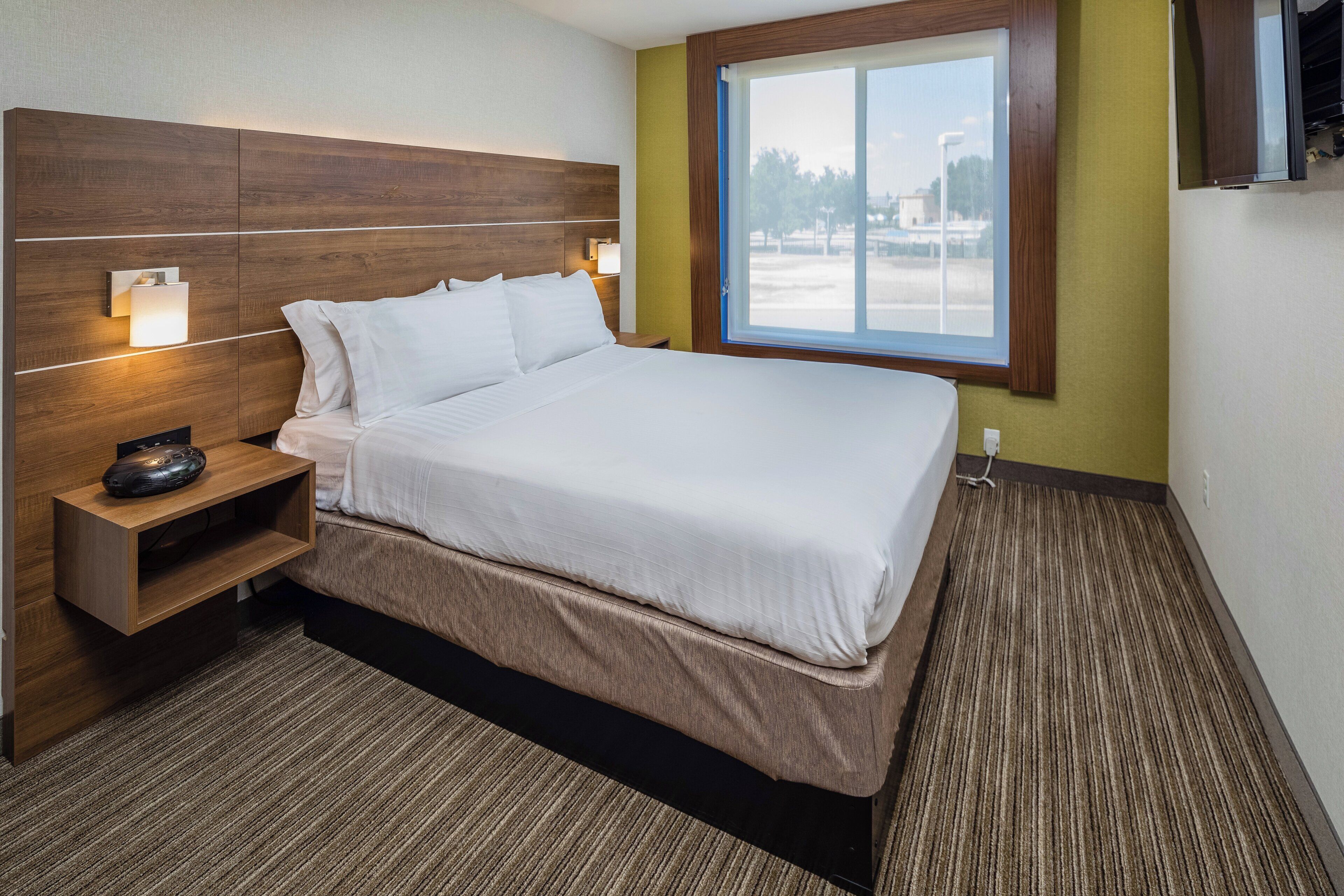 Habitación de hotel con cama, lámparas de noche, mesita de noche con control remoto y ventana con vistas al exterior.