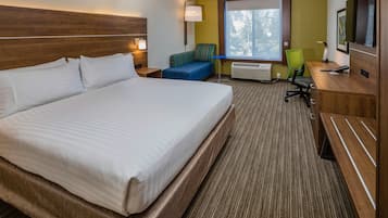 A hotel room with a large bed, a desk with a chair, a TV, and a window with a view of trees.