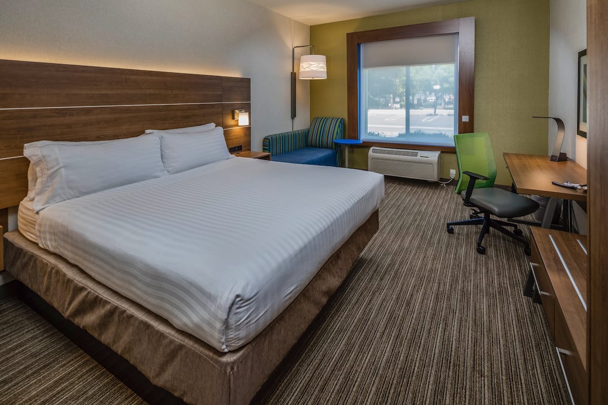 A hotel room with a large bed, a desk, a chair, and a window with a view of the outdoors.