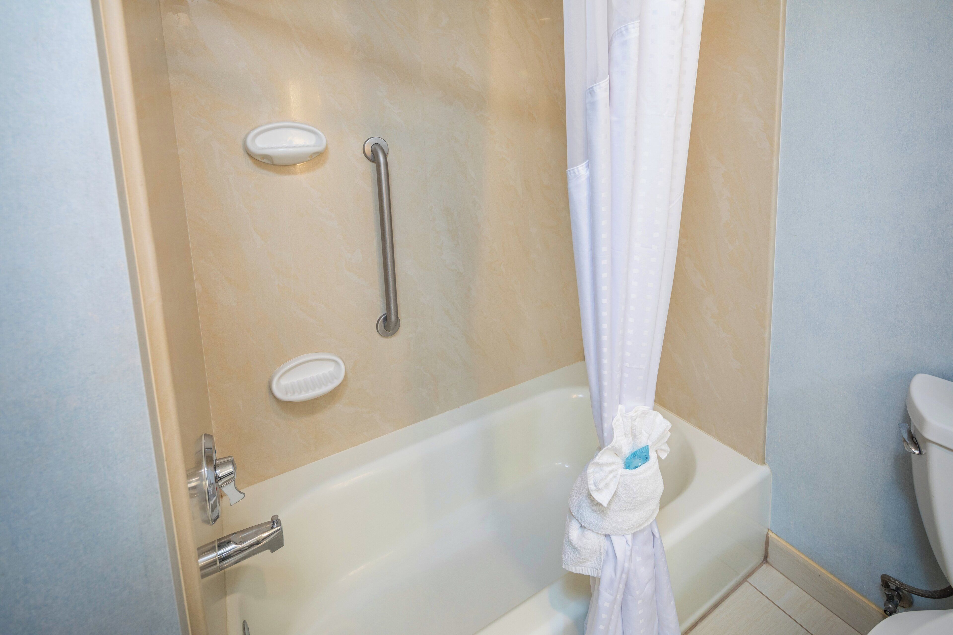 A bathroom with a bathtub, a shower, a toilet, and a handrail.