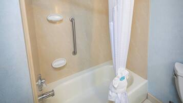A bathroom with a bathtub, a shower, a toilet, and a handrail.