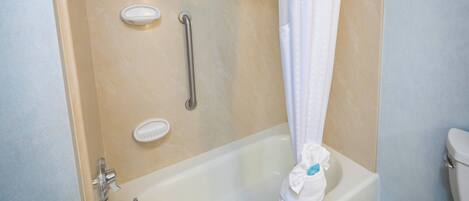 A bathroom with a bathtub, a shower, a toilet, and a handrail.