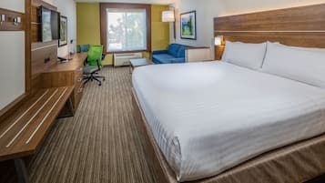 Ein Hotelzimmer mit einem großen Bett, einem Schreibtisch mit Stuhl, einem Fernseher und einem Fenster mit Blick auf Bäume.