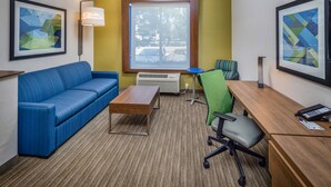 A hotel room with a blue sofa, a wooden desk, a green chair, and a large window with a view of the outdoors. - Holiday Inn Express and Suites Modesto by IHG (Modesto)