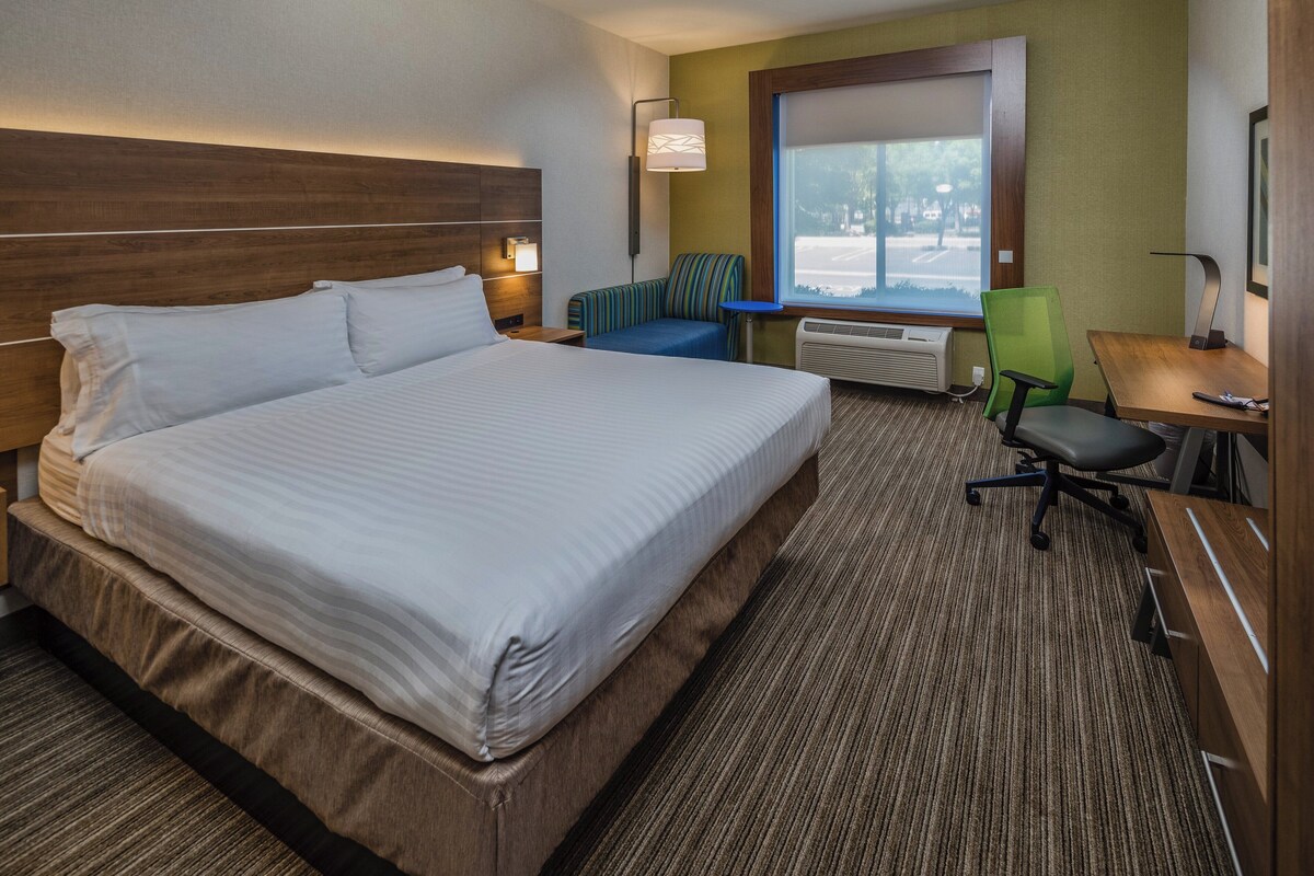 Une chambre d’hôtel avec un grand lit, un bureau, une chaise, une lampe et une fenêtre.