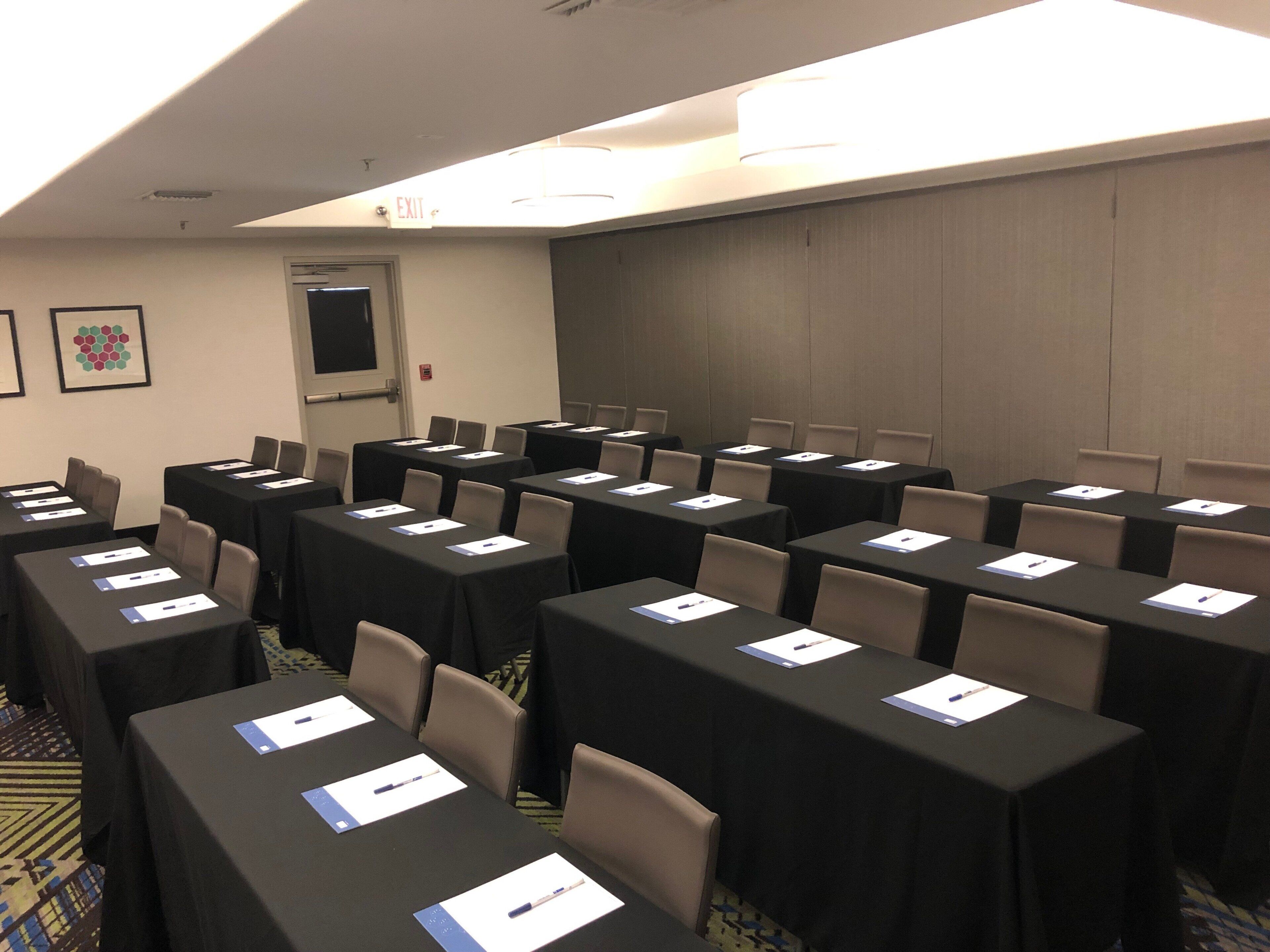 A conference room with multiple tables, chairs, and an exit sign.