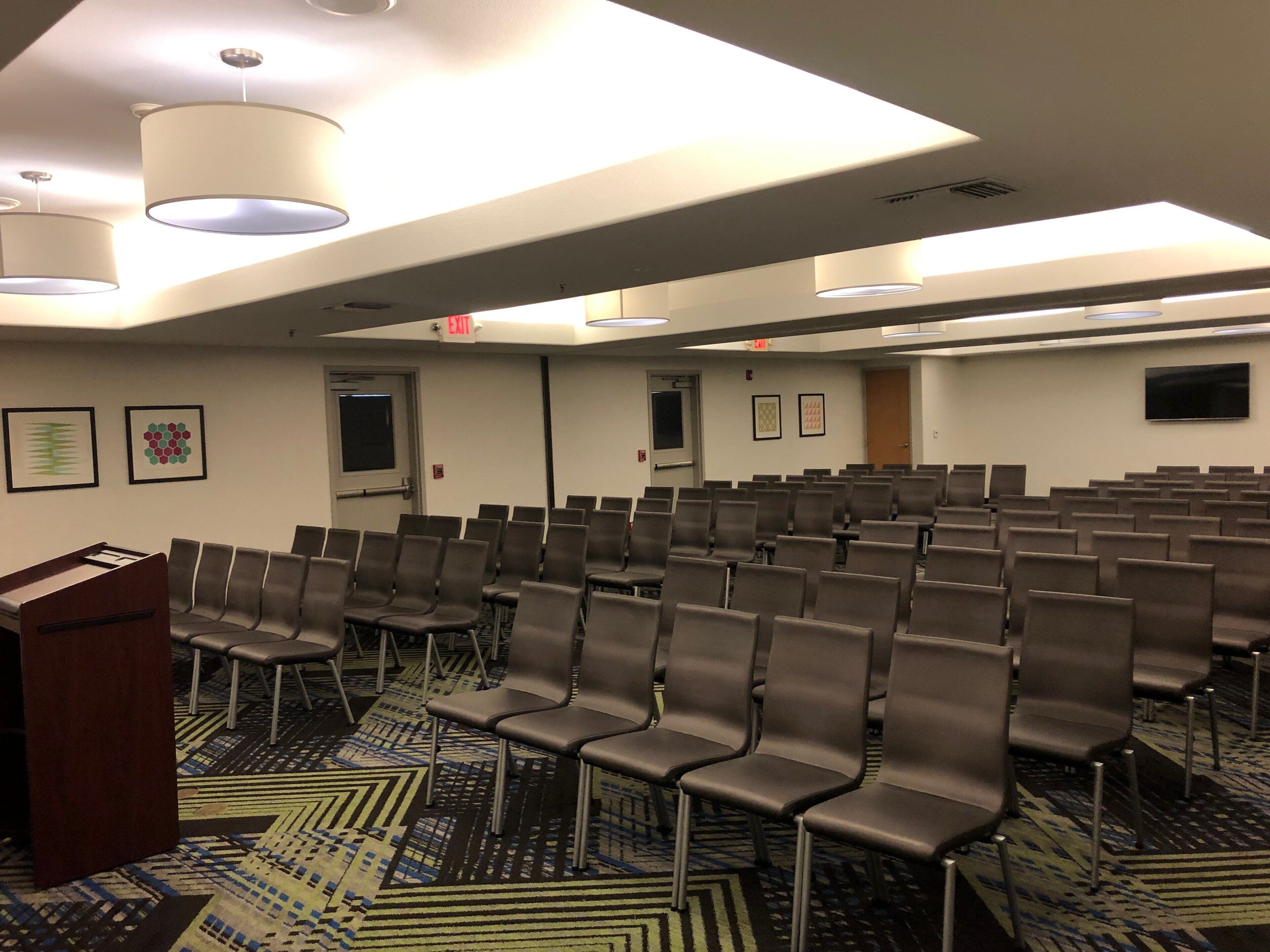 A conference room with rows of chairs, a podium, and framed artwork on the walls.
