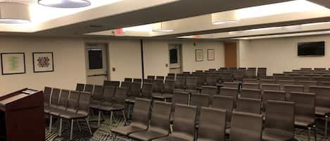 A conference room with rows of chairs, a podium, and framed artwork on the walls.