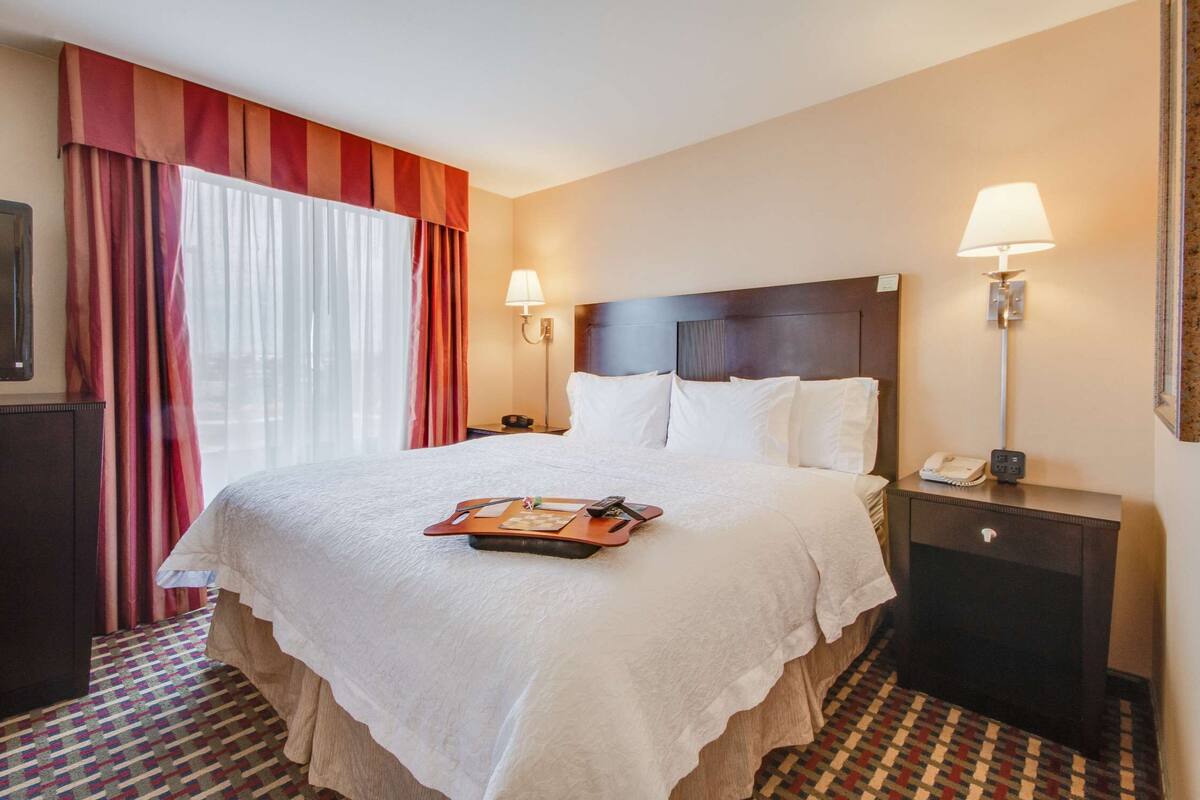 A hotel room with a large bed, two bedside lamps, a nightstand, and a TV on the left.